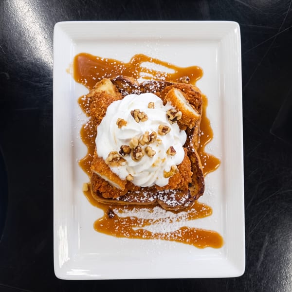 Chicken and waffles topped with whipped cream, walnuts, caramel, and powdered sugar.
