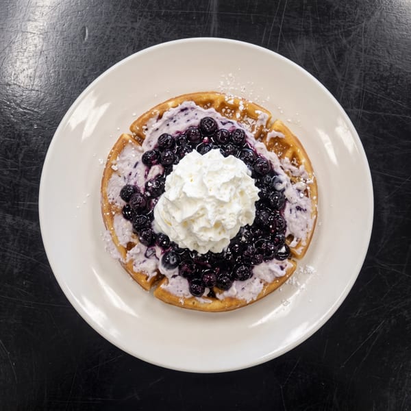 Golden waffle topped with blueberry cream, fresh blueberries, and whipped cream on a white plate.