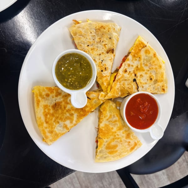 Golden-brown quesadilla wedges arranged on a white plate with small bowls of green and red salsa.
