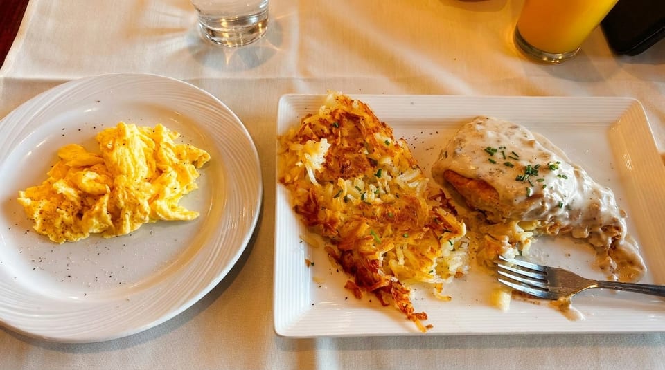 A breakfast plate with scrambled eggs, crispy hash browns, and biscuits and gravy.