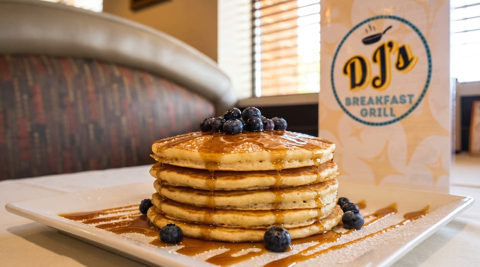 Stack of blueberry pancakes with syrup and powdered sugar on a white plate at DJ's Breakfast Grill.