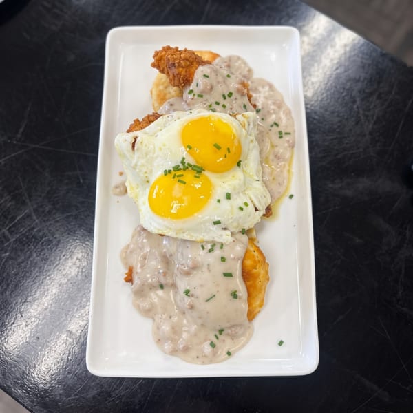 Fried chicken and biscuits covered in gravy and topped with two sunny-side-up eggs.